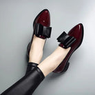 Shiny burgundy patent leather loafers with black bow detail, worn with black leggings. Stylish women's footwear, elegant design, fashion shoes.