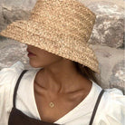 Woman wearing a wide-brimmed raffia straw hat, perfect for summer beach vacations, featuring a flat top design and UV protection.
