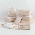 Beige travel packing cubes set with drawstring bag, transparent toiletry pouch, and white sneakers. Ideal for organized luggage and efficient packing.