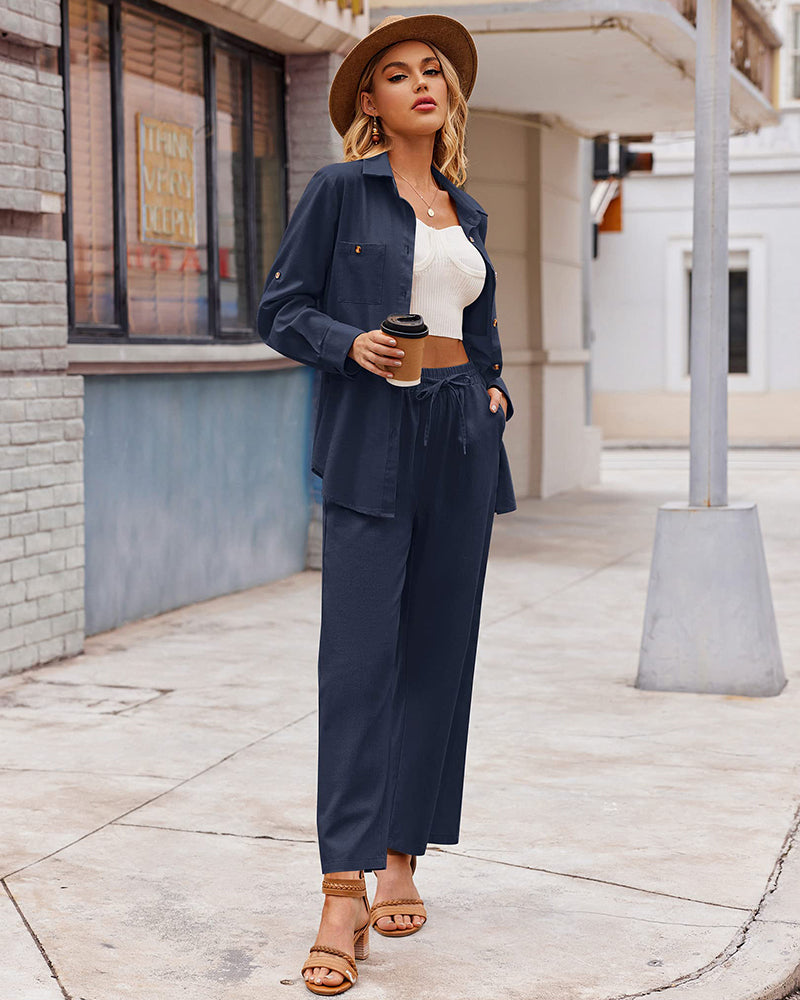 Woman in stylish navy blue pantsuit with white crop top, holding coffee cup, wearing straw hat and sandals, urban street background. Fashionable outfit.