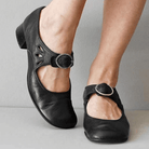 Black leather Mary Jane shoes with buckle strap and cutout design, worn on feet. Comfortable women's footwear, stylish and versatile for casual wear.