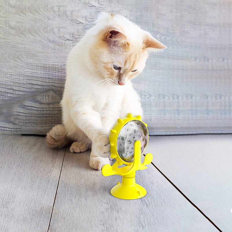 Cream-colored cat playing with a yellow interactive cat toy on a wooden floor. Cat toy with suction cup base and spinning wheel for pet entertainment.