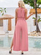 Woman in a pink halter-neck jumpsuit by a poolside, showcasing summer fashion. Elegant resort wear, perfect for vacation or beach outings.