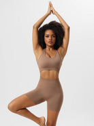 Woman in brown yoga set performing tree pose; activewear, fitness, yoga clothing, workout outfit, seamless sports bra and shorts.