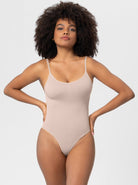 Woman wearing a beige seamless bodysuit with spaghetti straps, showcasing a minimalist design. Fashionable women's clothing, comfortable fit.