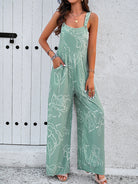 Woman wearing a stylish green floral jumpsuit with wide legs, standing against a white textured wall. Fashionable summer outfit, casual chic style.