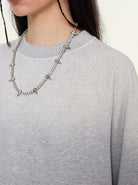 Woman wearing a gray sweatshirt and a silver spiked chain necklace. Fashionable casual outfit, trendy jewelry, modern street style accessory.