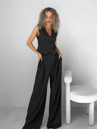 Woman in a stylish black pinstripe jumpsuit standing next to a modern white chair, showcasing trendy women's fashion and elegant outfit ideas.