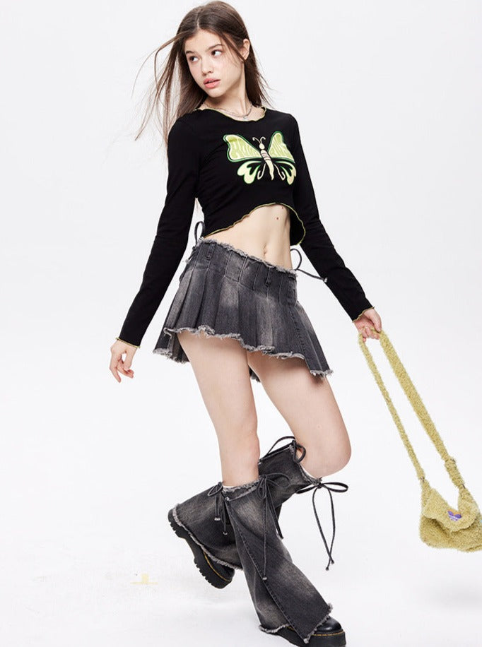 Young woman in a black butterfly crop top, gray pleated mini skirt, and oversized boots, holding a yellow textured handbag against a white background.