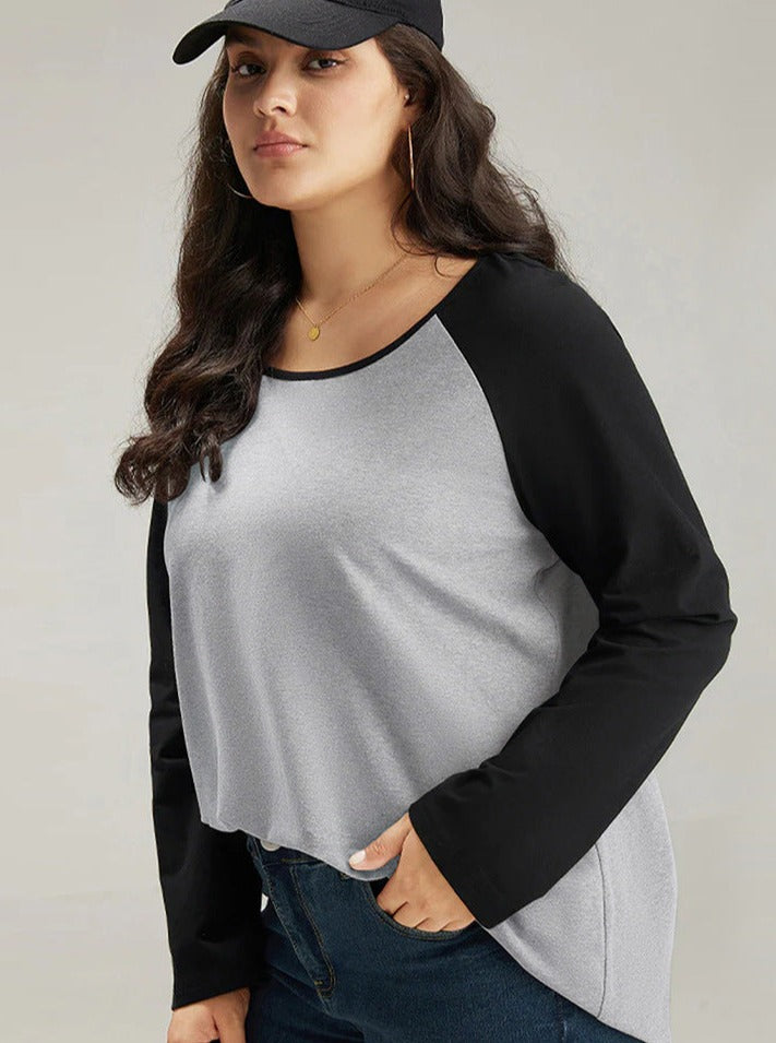 Woman wearing a casual gray and black long-sleeve raglan shirt, black cap, and jeans. Fashionable plus-size clothing, relaxed style.