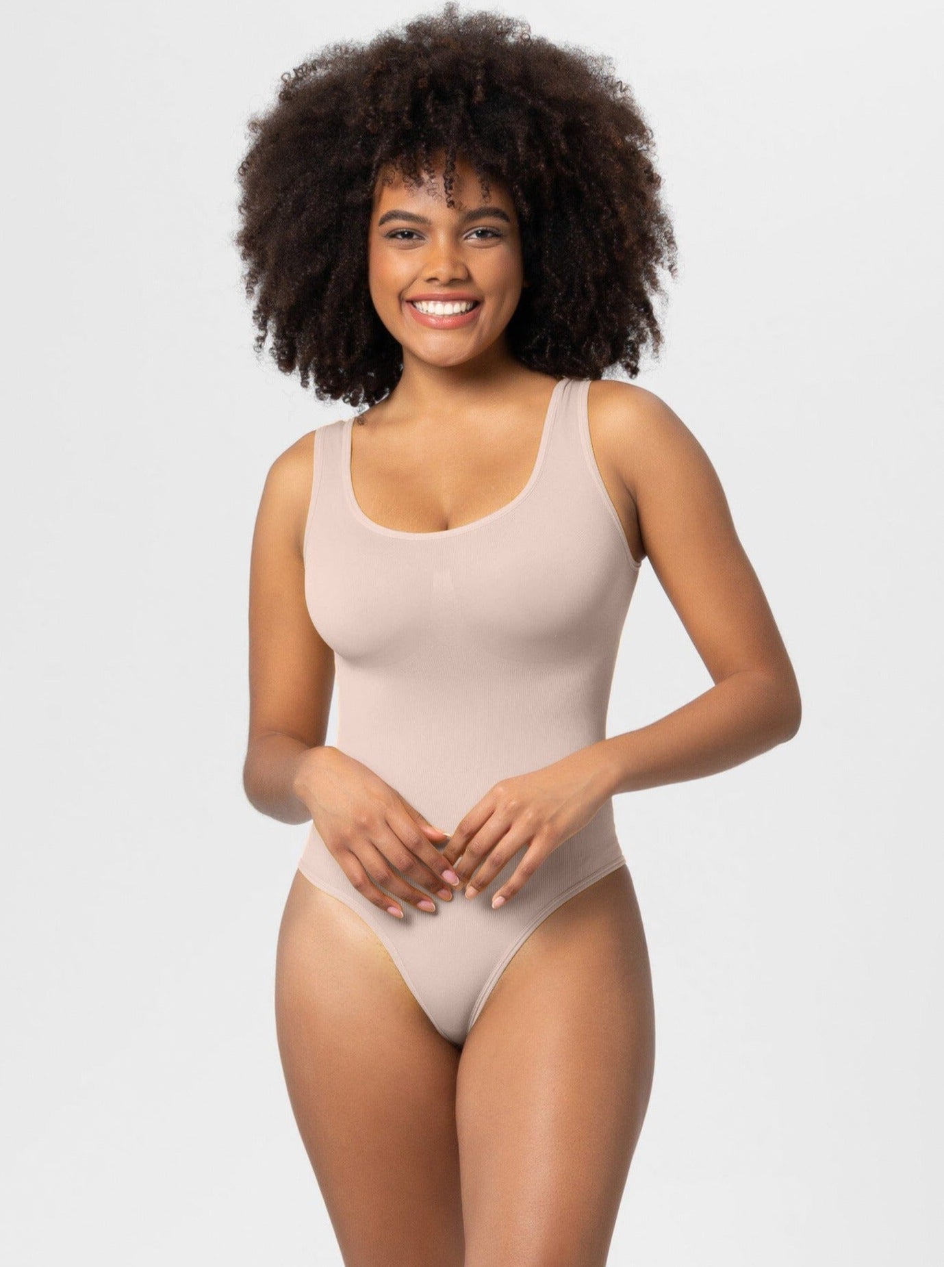 Woman wearing a beige seamless bodysuit with scoop neck, smiling against a white background. Comfortable, stylish women's shapewear.