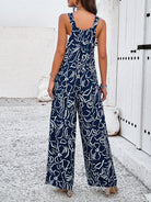 Woman wearing a navy blue and white abstract print jumpsuit, standing outdoors on a textured surface, showcasing summer fashion style.