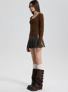 Woman in brown long-sleeve top, black pleated mini skirt, knee-high brown boots, and glasses. Fashionable fall outfit, side profile.