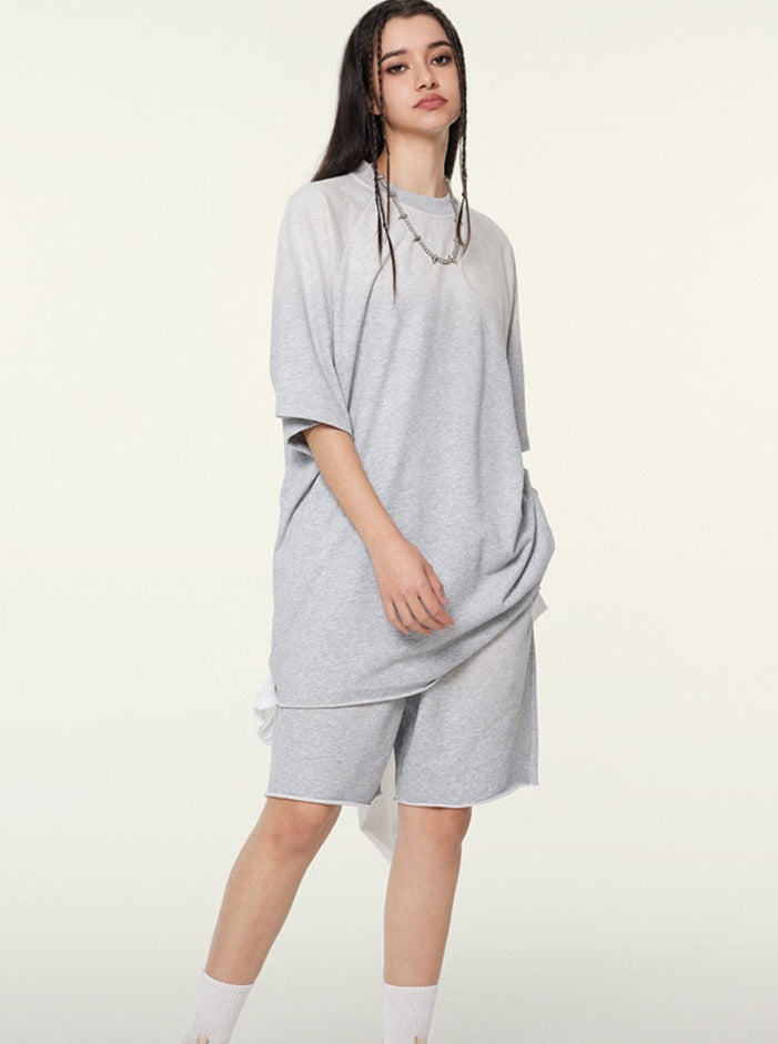 Woman in oversized gray t-shirt and shorts set, casual streetwear fashion, minimalist style, standing against a plain background.