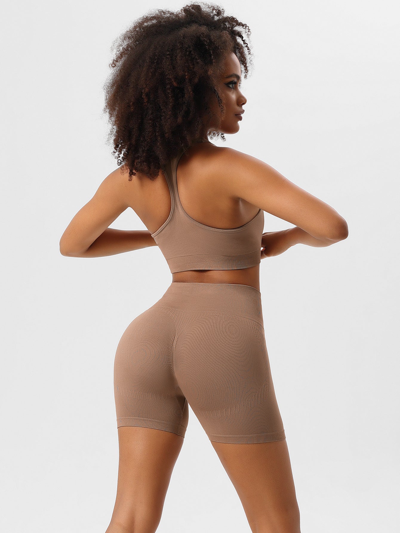 Woman in seamless brown activewear set, featuring a sports bra and high-waisted shorts, ideal for yoga and fitness. Comfortable, stylish workout outfit.