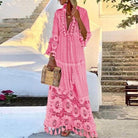 Woman in a pink bohemian maxi dress with lace details, holding a woven handbag, standing on stone steps. Summer fashion, boho style, vacation outfit.