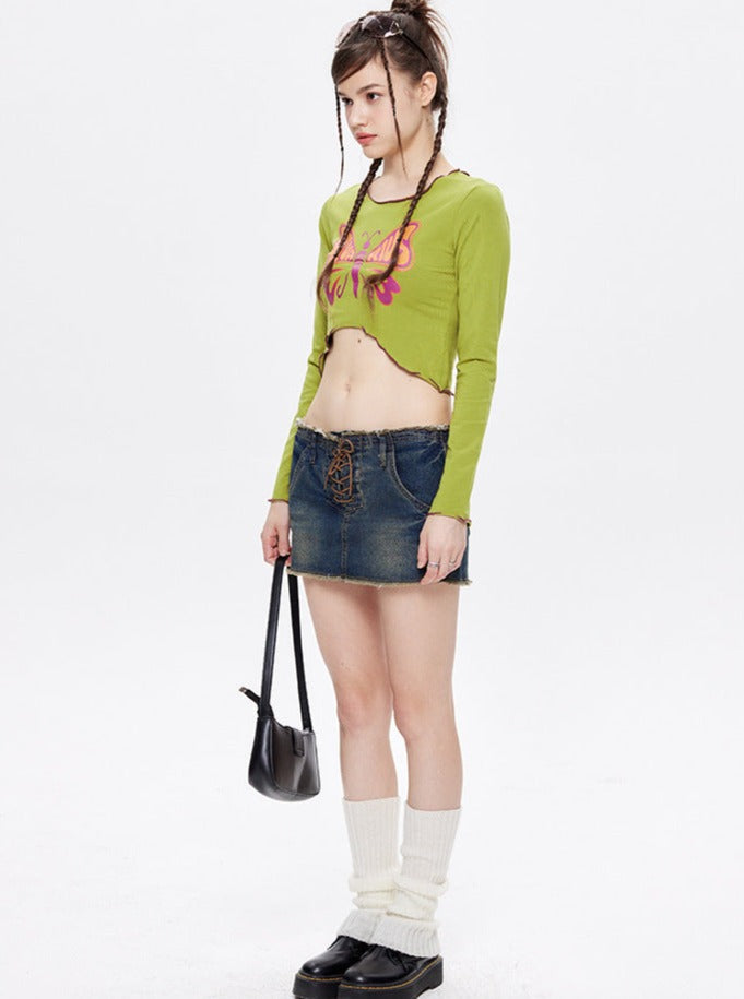 Young woman in a green crop top and denim mini skirt, holding a black handbag. Fashionable outfit with white leg warmers and black platform shoes.