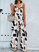 Woman wearing a stylish geometric print jumpsuit with a woven straw bag, standing against a white textured wall. Fashionable summer outfit.