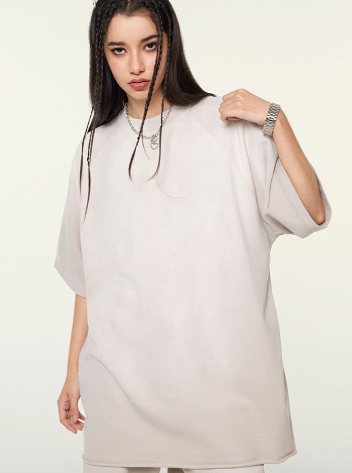 Young woman in oversized beige t-shirt with braided hair, wearing a silver chain necklace and watch, standing against a plain background. Fashion, casual wear.