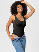 Woman in black sleeveless bodysuit and blue jeans, smiling confidently. Fashionable casual wear, stylish outfit, trendy clothing.