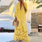 Woman in a yellow bohemian maxi dress with lace details, holding a wicker handbag, standing on a stone pathway. Summer fashion, boho style.
