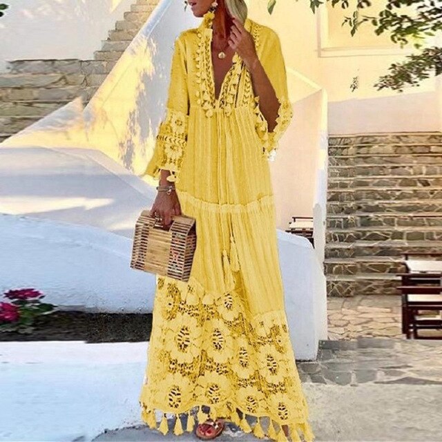 Woman in a yellow bohemian maxi dress with lace details, holding a wicker handbag, standing on a stone pathway. Summer fashion, boho style.