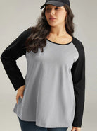 Plus-size woman in a casual gray and black long-sleeve raglan top, wearing a black cap and jeans. Fashionable, comfortable, everyday wear.