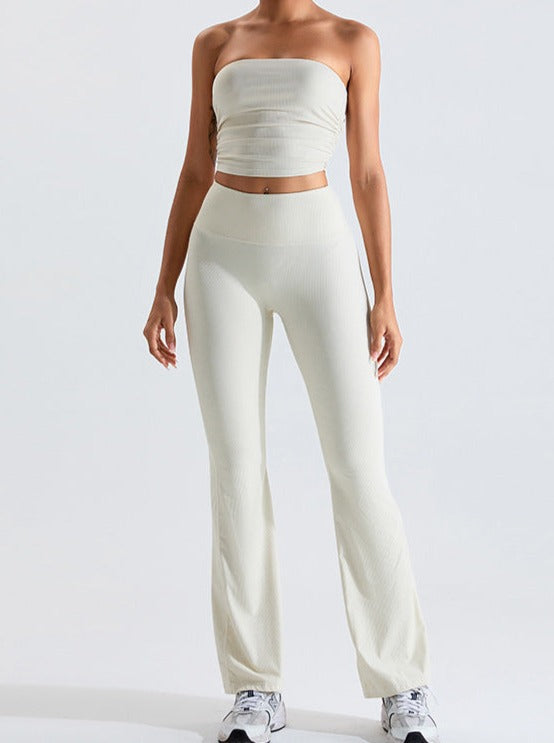 Woman wearing a white ribbed tube top and matching high-waisted flared pants, showcasing trendy minimalist fashion.