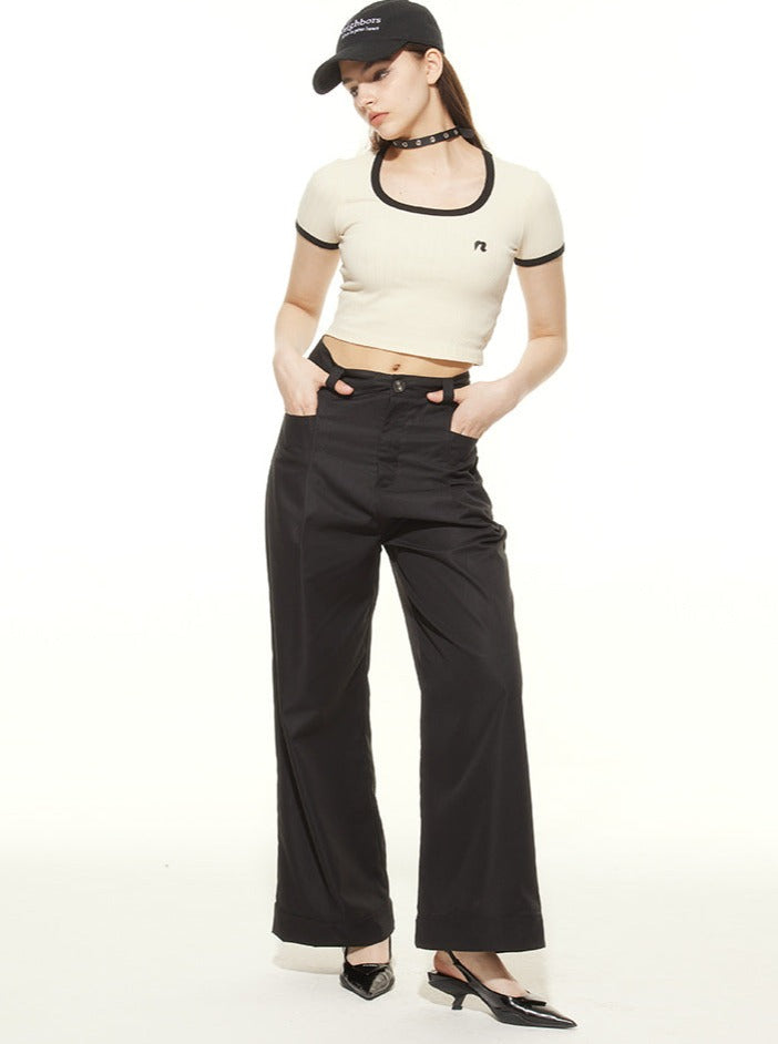 Woman in stylish casual outfit featuring a white crop top, black wide-leg pants, and a black cap. Fashionable streetwear look for women.