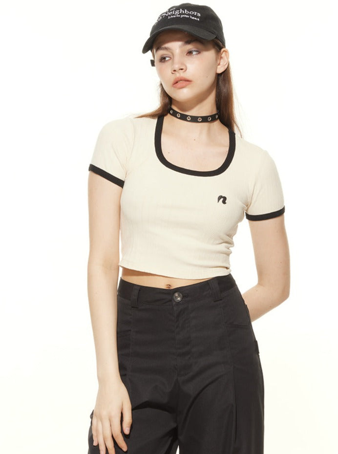 Young woman in a stylish beige crop top with black trim, black high-waisted pants, and a black cap. Fashionable casual outfit, trendy streetwear.