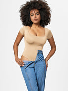 Woman in beige bodysuit and blue jeans, curly hair, fashion model, studio portrait, casual style, trendy outfit, confident pose, white background.