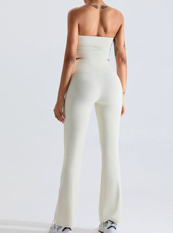 Woman in white ribbed two-piece outfit, featuring a strapless top and high-waisted flared pants, showcasing trendy fashion style.