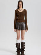 Woman in brown long-sleeve top, black pleated mini skirt, knee-high brown boots, and glasses. Fashionable outfit, modern style, casual wear.