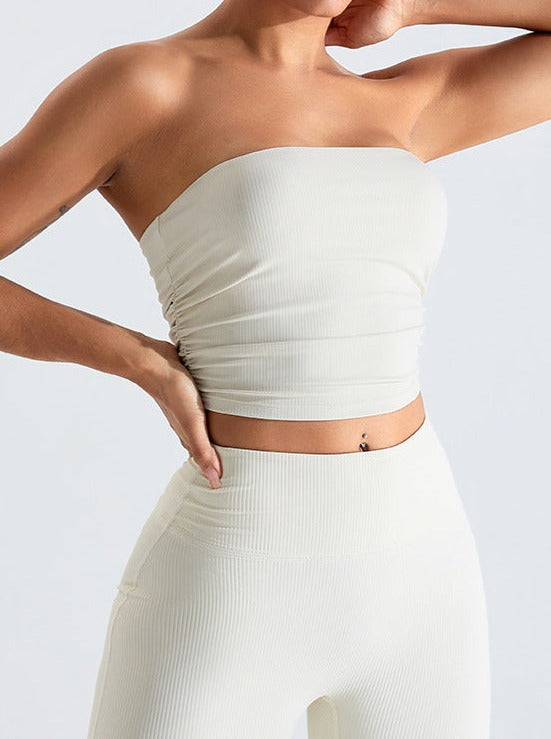 Woman wearing a white ribbed strapless crop top and matching high-waisted leggings, showcasing trendy minimalist fashion and comfortable activewear.