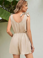 Woman wearing a beige sleeveless romper with bow-tie shoulder straps, standing outdoors. Fashionable summer outfit, casual chic style.