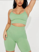 Woman in green workout set, featuring a crop top and high-waisted shorts, posing against a white background. Fitness fashion, activewear.