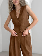 Woman wearing brown pinstripe vest and pants set, featuring button-up design and sleeveless cut, accessorized with silver necklace and bracelet.