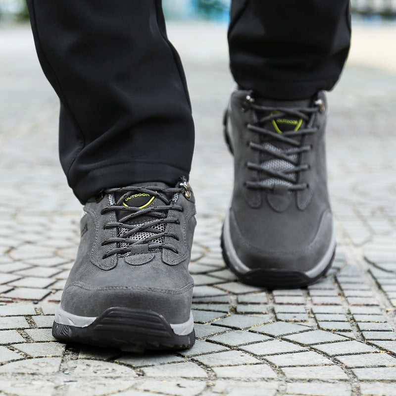 Gray outdoor hiking boots with durable soles and lace-up design, worn by a person walking on a cobblestone path. Ideal for trekking and adventure.