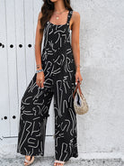 Woman wearing a stylish black and white abstract print jumpsuit, accessorized with bracelets and a woven handbag, standing against a textured wall.