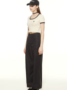 Woman in casual outfit wearing a beige crop top, black wide-leg pants, black cap, and choker. Fashionable streetwear style for women.