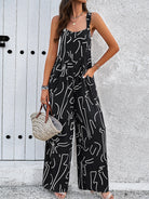 Woman wearing black abstract print jumpsuit with pockets, holding a woven handbag. Fashionable summer outfit against a white textured wall.