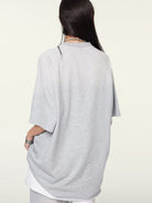 Gray oversized T-shirt on woman, back view. Casual fashion, loose fit, comfortable style. Ideal for streetwear, everyday wear, minimalist wardrobe.