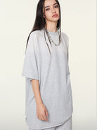 Woman in oversized gray t-shirt with braided hair, standing against a plain background. Fashionable casual wear, minimalist style, streetwear.