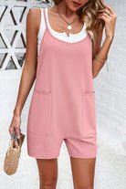 Woman in pink sleeveless romper with front pockets, holding a woven handbag. Casual summer fashion, stylish outfit, white brick background.