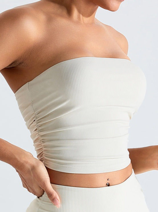 Woman wearing a white strapless ribbed tube top with ruched sides, showcasing trendy summer fashion. Perfect for casual and stylish outfits.