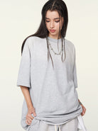 Young woman in oversized gray t-shirt with braided hair, looking down. Casual fashion, streetwear style, neutral background.