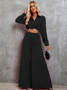 Woman in elegant black two-piece outfit with long sleeves and wide-leg pants, holding a stylish clutch. Fashionable attire for evening events.