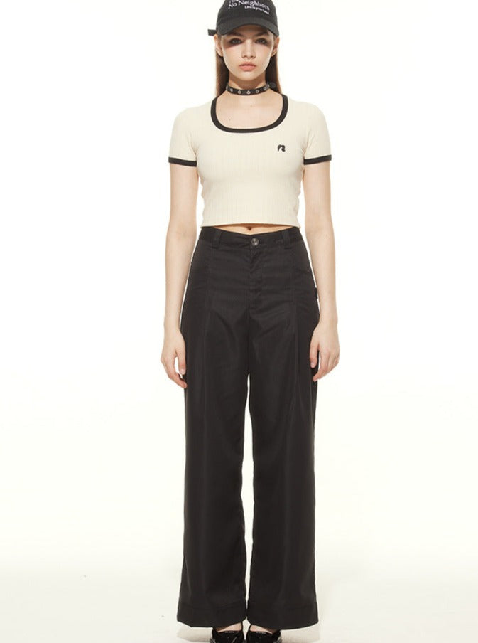 Young woman in a stylish outfit featuring a white crop top, black wide-leg pants, and a black cap. Fashionable streetwear look, modern casual style.