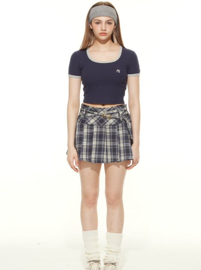 Teen girl in navy crop top, plaid skirt, and headband, standing against white background. Fashionable casual outfit, youthful style, trendy clothing.