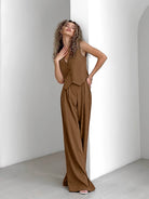 Woman in stylish brown pinstripe vest and wide-leg pants set, standing in a minimalist white room. Fashionable outfit, modern women's clothing.